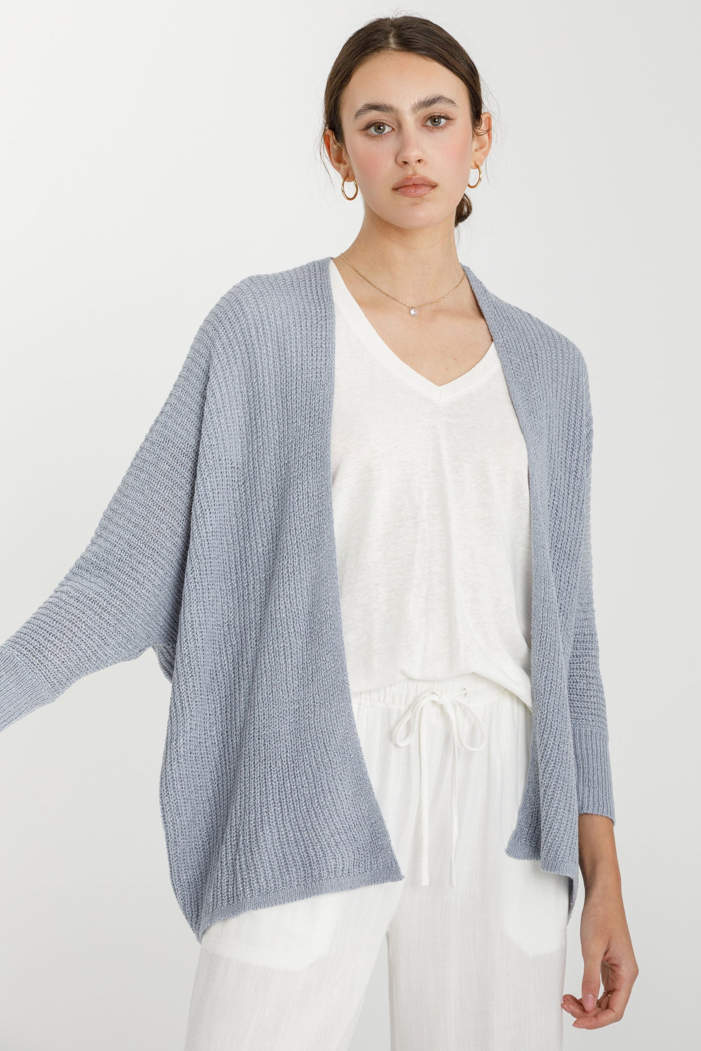 Woman wearing a dusty blue open front cardigan over a white top and pants