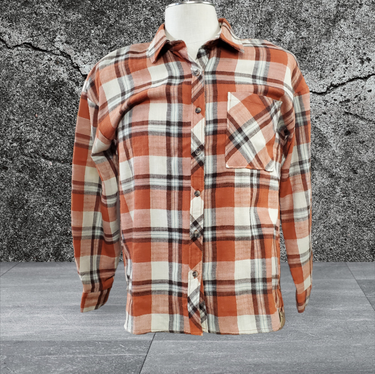 Oversized boyfriend flannel shirt with a brick plaid pattern, featuring a turn-down collar, drop shoulder, and open pocket, displayed on a mannequin against a concrete and stone backdrop.