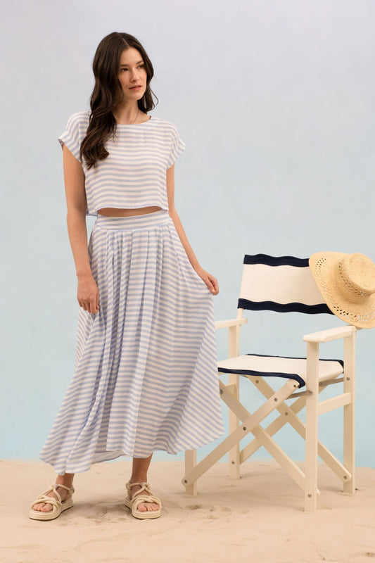 Woman in striped outfit standing next to a director's chair with a straw hat on a light blue background